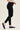 A model wearing black skinny jeans and navy blue Mary Jane flats, shown from the waist down in a side profile against a light beige studio background.