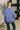 A woman viewed from behind wearing a dusty periwinkle blue crewneck sweatshirt and dark blue jeans in a modern indoor setting.