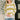 A woman wearing a cream and olive green striped knit sweater with a white collar, paired with blue jeans, standing in a brightly lit indoor setting.