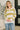 A woman wearing a cream and olive green striped knit sweater with a white collar, paired with blue jeans, standing in a brightly lit indoor setting.