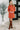 Woman wearing an orange dress with buttons and brown knee-high boots indoors.
