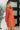 Woman wearing an orange dress with buttons in a minimal indoor setting.