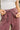 A close-up of a person wearing dusty rose drawstring sweatpants and a white tank top, adjusting the drawstring at the elastic waist.