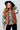 Woman wearing a patterned sweater with a brown vest and black hat against a white tiled wall.