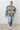 Person wearing a colorful patterned sweater and light blue jeans against a white wall.