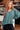 Woman wearing a teal sweater and black pants in an indoor setting