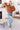 Woman in orange sweater and blue jeans standing in a living room.