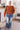 Woman wearing a rust-colored sweater and blue jeans standing in a living room.