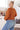 Woman wearing an orange sweater and blue jeans in a kitchen setting