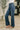 A person wearing dark blue high-waisted flare jeans, styled with a white top and pink block-heel mules, standing on a patterned rug in an indoor setting.