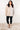 Woman wearing a striped sweater and black leggings against a white wall.