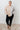 Person wearing a striped sweater and black leggings standing against a white paneled wall.