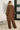 Person wearing a brown outfit standing in a room with a plant and sofa.