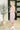 Woman in a sleeveless dress standing in an indoor setting with a plant and door in the background.