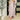 A woman models a dusty rose knit mock-neck midi dress with long draped sleeves, styled with a white belt and white ankle boots in a modern indoor setting.