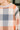 Close-up of a person wearing a long-sleeve plaid top with peach, gray, and off-white check blocks, plus a striped and textured sleeve detail.