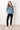 Woman wearing a blue cable knit sweater and black leggings against a white tiled wall.