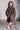 Child wearing a leopard print poncho standing against a white brick wall.