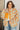 Woman wearing a floral jacket with orange flowers, yellow shirt, and blue jeans.