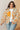 Woman wearing a floral jacket with orange flowers and a white shirt underneath, standing against a neutral background.