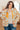 Woman wearing a floral patterned jacket with an orange interior, standing indoors.
