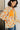Woman wearing a floral jacket with orange flowers against a white wall.