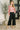 Woman wearing a colorful floral blouse and black pants in an indoor setting.