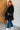Person wearing a black oversized sweater and blue jeans against a white brick wall.