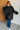 Person wearing a black coat standing against a white brick wall.