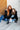 Two women sitting on a floor against a white brick wall.
