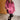 Woman wearing a pink oversized hoodie in a room with wooden floor and white brick wall.