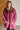Woman wearing a pink fleece hoodie standing against a white brick wall.