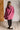 Person wearing a pink hooded garment against a white brick wall.