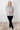 Woman wearing a black and white floral blouse with black pants against a white tiled wall.