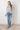 Woman wearing a patterned blouse and jeans against a white tiled wall.