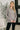 Woman wearing a gray sweater standing indoors with decorative elements in the background