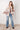 Woman wearing a patterned jacket and jeans standing against a white tiled wall.
