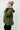 Woman wearing an olive green jacket against a white tiled wall
