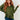 A woman with long wavy red hair wearing an olive green long-sleeve polo-style top and blue jeans, standing against a white paneled wall.