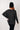 Person wearing a dark gray cardigan and black beanie against a white paneled wall.