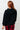 Person wearing a black textured sweater and red plaid pants against a white tiled wall.