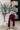Woman wearing a black floral blouse and burgundy pants in an indoor setting.