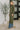 Woman wearing a long green dress with blue jeans indoors.