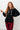 Woman wearing a black textured hoodie and red plaid pants against a white wall.