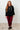 Woman wearing a black hoodie and red plaid pants standing against a white wall.