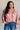 Woman wearing a floral blouse and jeans against a white brick wall.