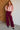 Woman wearing a floral blouse and burgundy pants against a white brick wall.