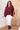 Woman wearing a burgundy top and white pants indoors.