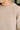 Close-up of a person wearing a light beige knit sweater, showing the ribbed crew neck, textured knit fabric, and shoulder seam.