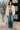 Woman wearing a beige jacket, striped sweater, and blue jeans indoors.